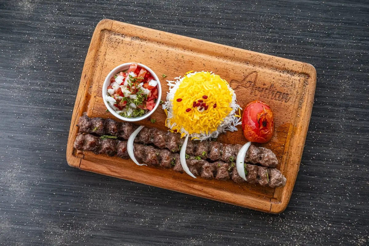 Koobideh kebab plated with saffron rice and grilled tomato